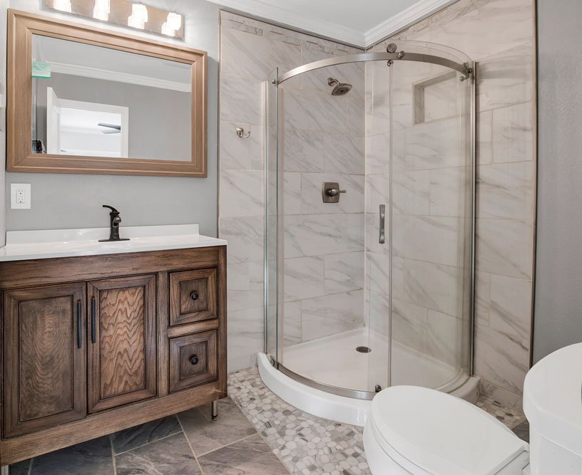 A modern bathroom design featuring a spacious glass-enclosed corner shower with sleek, polished chrome hardware.